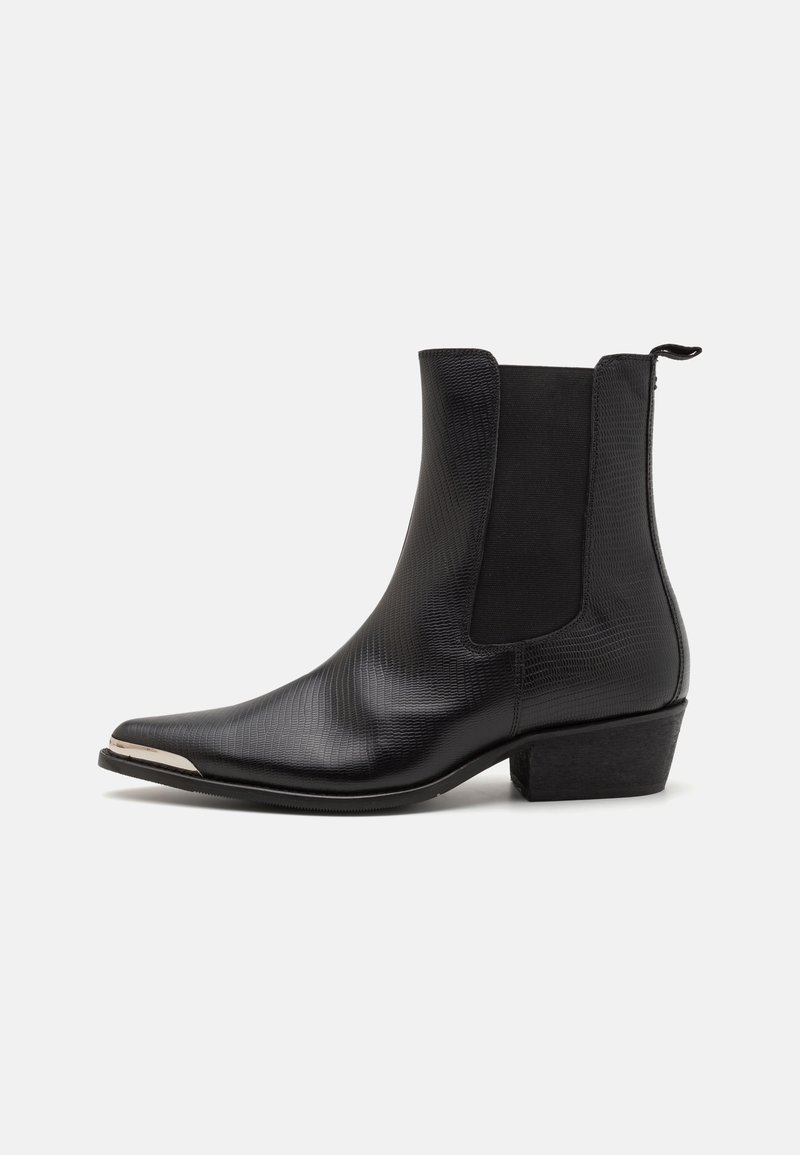 Bottine en cuir noir texturé avec bout pointu, embout en métal argenté, panneaux élastiques sur les côtés et petit talon carré sur fond blanc.