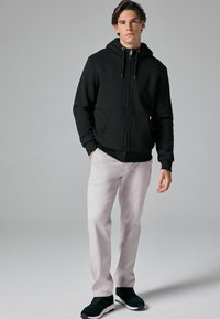 Sort zip-up hoodie med kengurulommer, parret med lyse grå bukser og sorte sportssko. Enkel design og komfortabel pasform.