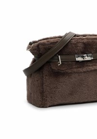 Ruskea shearling-laukku, jossa on jämäkkä muoto, nahkahihna ja hopeinen solki. Sen pehmeä rakenne ja minimalistinen muotoilu ovat sen erikoisuus.