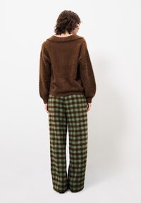 Braun-flauschiger Pullover mit einem breiten Kragen, kombiniert mit grünen und braunen karierter weit geschnittenen Hosen mit einem schachbrettartigen Muster.