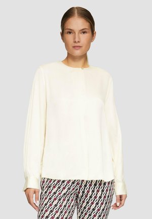 Crème-kleurige blouse met lange mouwen, ronde halslijn en een subtiele knoopdetail bij de hals. Glad materiaal met een vloeiende val.