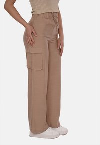 Pantaloni cargo beige con vestibilità rilassata, vita elastica e dettagli con tasche laterali. Realizzati in un tessuto leggero, abbinati a sneakers bianche.