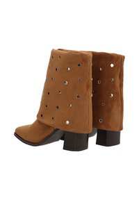 Botines de ante marrón con punta afilada, que presentan tachuelas de metal plateado y un tacón grueso. Superficie texturizada y diseño de caña corta.