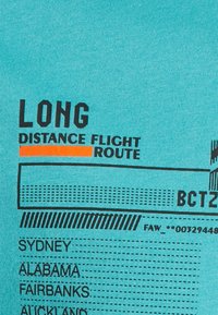 Turkos tyg med svart text som visar "LÅNGDISTANSFLYG RUTT." Inkluderar stadnamn och prickade linjer, med en orange accent.