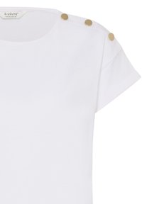 Chemise blanche à manches courtes avec encolure ronde et trois boutons dorés le long de la couture de l'épaule gauche.