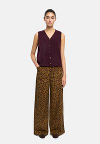 Burgundowa bezrękawnik z dzianiny z guzikami z przodu, w połączeniu z szerokimi brązowymi spodniami w czarne kropki. Prosty, casualowy design.