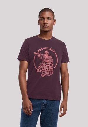 Bordeauxfarbene Baumwoll-T-Shirt mit einem grafischen Druck eines Mannes mit Sonnenbrille, darauf "ROCKET MAN" und "Elton John" in pinkfarbigem, stilisiertem Text. Kurze Ärmeln.