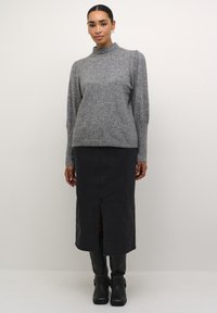 Szürke kötött pulóver magas nyakkal, fekete farmer szoknyával, amely elöl hasítékkal rendelkezik, és térd fölé érő fekete bőr csizmával párosítva.