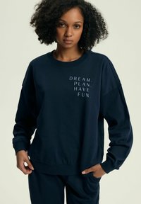 Granatowy sweter z okrągłym dekoltem, długimi rękawami i białym napisem: "SPEŁNIAJ MARZENIA. PLanuj. Ciesz się." Miękki bawełniany materiał o luźnym kroju.