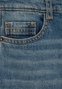 Denim tkanina v svetlo modri barvi z obrabljenim videzom. Ima sprednji žep s kontrastnim oranžnim šivanjem in kovinsko gumbno podrobnostjo.