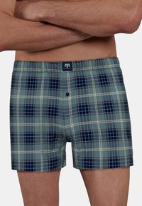 Boxers de cuadros azules que presentan una mezcla de cuadrados en tonos claros y oscuros de marino con acentos crema, cinturilla elástica y un cierre de un solo botón.