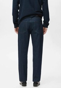 Dark blue jeans with a straight leg design and two back pockets. The fabric appears durable with a subtle texture. Paired with black shoes.