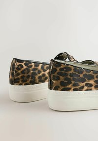 Pár nízkych tenisk s leopardím vzorom na látkových vrchoch a hrubými bielymi gumovými podrážkami na jednoduchom pozadí.