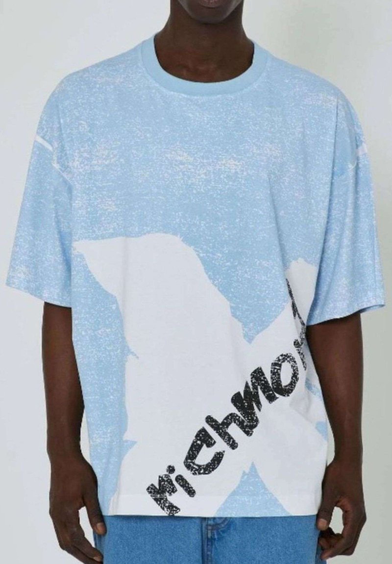 T-shirt overdimensionato di colore azzurro chiaro con motivo astratto bianco e testo nero, caratterizzato da un colletto rotondo e maniche corte.
