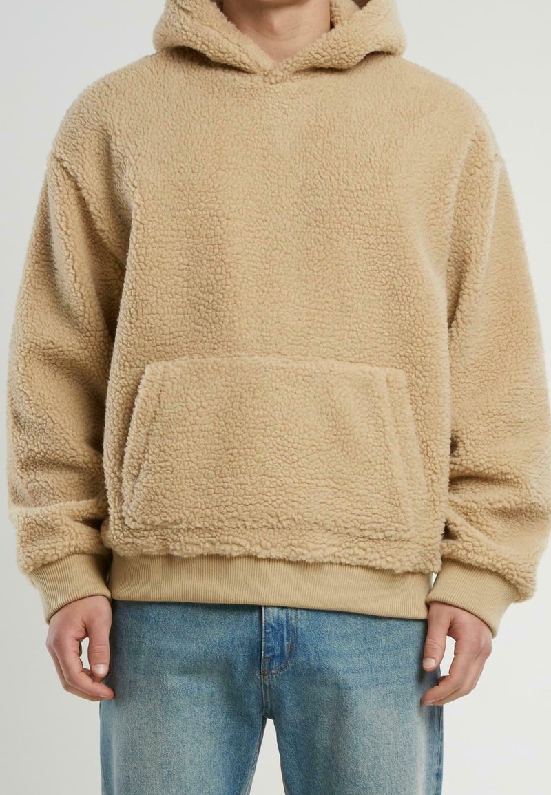 Sudadera de felpa beige con una superficie texturizada y suave, un bolsillo tipo canguro en la parte frontal y puños y dobladillo acanalados. Diseñada en un corte holgado.