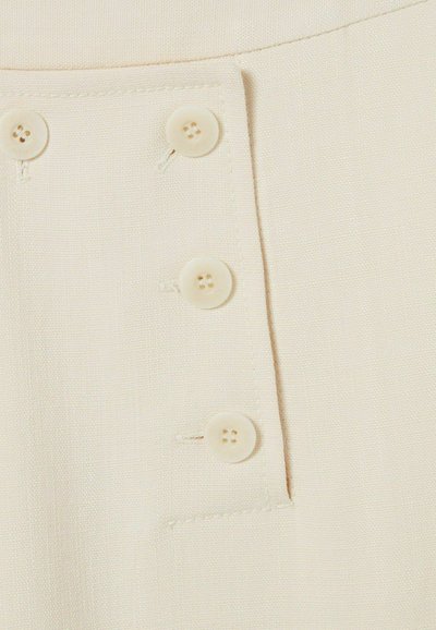 Gros plan sur un tissu beige présentant trois petits boutons ronds à quatre trous sur une patte de boutonnage verticale avec un subtil détail de couture.