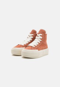 Zapatillas altas de ante rosa con cordones blancos, que presentan una gruesa suela de goma crema y detalles de costura visibles.