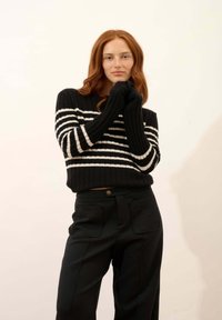 Czarny i biały sweter z dzianiny w paski o prążkowanej teksturze, z długimi rękawami, zestawiony z czarnymi spodniami typu high-waist z kieszeniami.