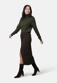 Groene coltrui en een chocoladebruine corduroy rok met een zijsplit, gecombineerd met donkere enkellaarsjes met een blokhak.