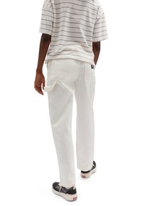 Vita cargobyxor med sidofickor och bälteshällor, i kombination med en randig kortärmad skjorta. Har en strukturerad tygkvalitet och en avslappnad passform.