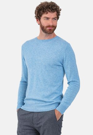 Pull tricoté bleu clair avec col rond, manches longues et ourlet côtelé ; porté sur un pantalon gris, présentant une texture douce.