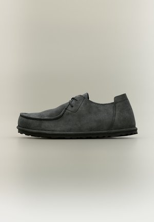 Chaussure décontractée pour homme en suède gris foncé à lacets, semelle épaisse et bout arrondi sur fond gris clair.
