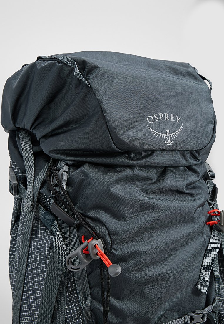 Zwarte Osprey wandelrugzak met bovenklep, verstelbare banden, rode koordsluitingen en voorste netvak.