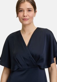 Marineblaues Wickelkleid mit kurzen, weiten Ärmeln und einem strukturierten Stoff. Der Ausschnitt ist tief V-förmig, und die Taille ist gerafft für eine taillierte Passform.