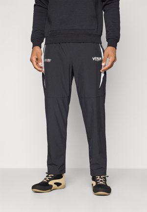 Black athletic pants with a smooth texture, featuring white side stripes, VENUM logo, and zippered pockets on the sides.