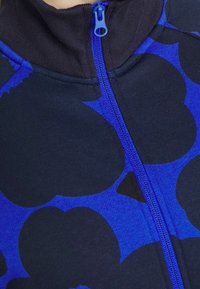 Chaqueta navy de cremallera con un atrevido patrón floral azul, tejido texturizado, cuello alto y cremallera azul en contraste.