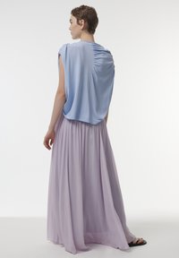Lichtblauw topje met gedrapeerde achterkant en korte mouwen, gecombineerd met een vloeiende lavendelkleurige maxirok. De outfit heeft zachte, lichte stoffen.