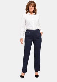 Navy geruite broek met een getailleerde pasvorm, voorzien van een platte voorkant, riemlussen en twee zijzakken, gecombineerd met een witte overhemdd.