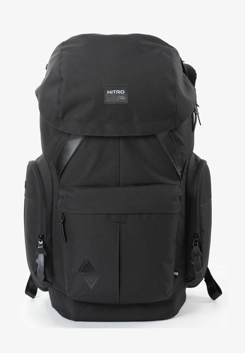 Sac à dos en tissu noir avec un rabat supérieur, des bretelles réglables, plusieurs compartiments zippés et un détail de logo texturé à l'avant.