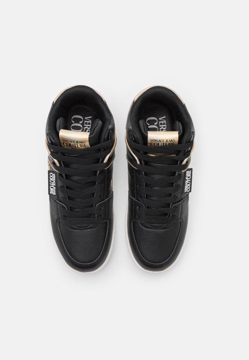 Un paio di sneakers alte nere Versace Jeans Couture con dettagli dorati e lacci neri, viste dall'alto su uno sfondo bianco.