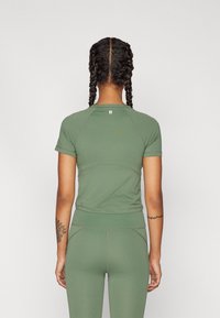 Krátký rukáv, přiléhavý, olivově zelený atletický top s raglánovými rukávy, bezešvým designem a malým logem na horní části zad.