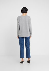 Grå huvtröja med avslappnad passform och långa ärmar, ihop med blå raka jeans och svarta klackmules, visad bakifrån.