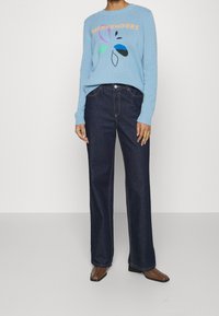 Pull en tricot bleu avec un graphique "WEEKENDERS", associé à un jean large en denim foncé. Les caractéristiques comprennent des poignets côtelés et des détails de couture.