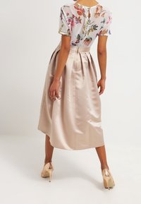 Květinová průsvitná blůza s krátkými rukávy spárovaná s béžovou saténovou midi sukní ve tvaru A, která má sklady a skrytý zip.