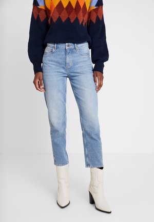 Jasnoniebieskie dżinsy o prostym kroju, z wyblakłym wykończeniem, z przeszytymi kieszeniami, zestawione z białymi botkami za kostkę z szpiczastym czubkiem i słupkowym obcasem.