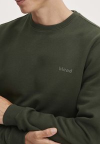 Donkergroene sweatshirt met ribbelkraag en -manchetten; heeft een subtiele "blend"-logo op de borst; zacht, textuurstoffen.