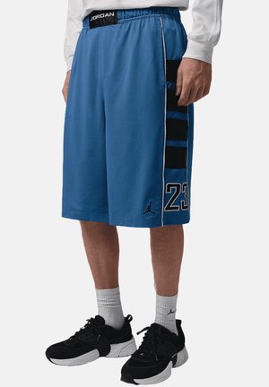 Mand iført blå Jordan basketballshorts med sorte og blå sidelister og sorte sneakers med hvide såler.