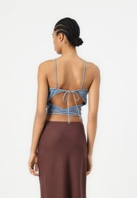 Denim crop top s podešavanjima na leđima, s izrezanim detaljima i uskim trakama, u kombinaciji s smešnim suknjom.