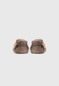 Zapatillas de fieltro marrón con rayas naranjas, de textura suave, talón redondeado y suela plana. Diseño minimalista adecuado para uso en interiores.