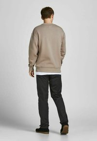 Grijze sweatshirt met een relaxed fit, ronde hals en geribbelde manchetten, gecombineerd met zwarte broek en zwarte schoenen, gezien vanaf de achterkant.