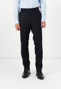 Marineblaue, maßgeschneiderte Hose mit geradem Schnitt, versehen mit Falten und einer glatten Textur. Getragen mit einem hellblauen Hemd und schwarzen Lederschuhen.