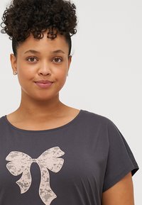 Dark gray short-sleeve t-shirt featuring a lace bow graphic in light pink at the center, with a relaxed fit and soft texture.
