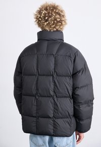 Giubbotto a vento nero con collo alto, caratterizzato da un design imbottito, texture morbida e pannelli cuciti orizzontalmente, visto da dietro.