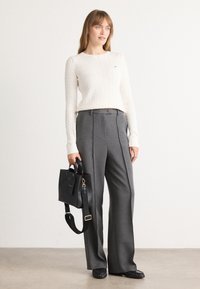 Crèmekleurige kabelgebreide trui, grijze op maat gemaakte wijde broek, zwarte handtas met schouderband, platte zwarte schoenen; minimalistisch ontwerp, geen patronen.