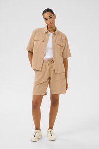 Lyhythihainen beige paita ja vastaavat shortsit kevyestä kankaasta, paidassa on tasku ja shortsien vyötäröllä joustava vyötärönauha.