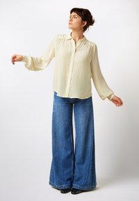 Light cream button-up shirt with puff sleeves, paired with high-waisted, wide-leg blue denim jeans. Soft texture and relaxed fit throughout.